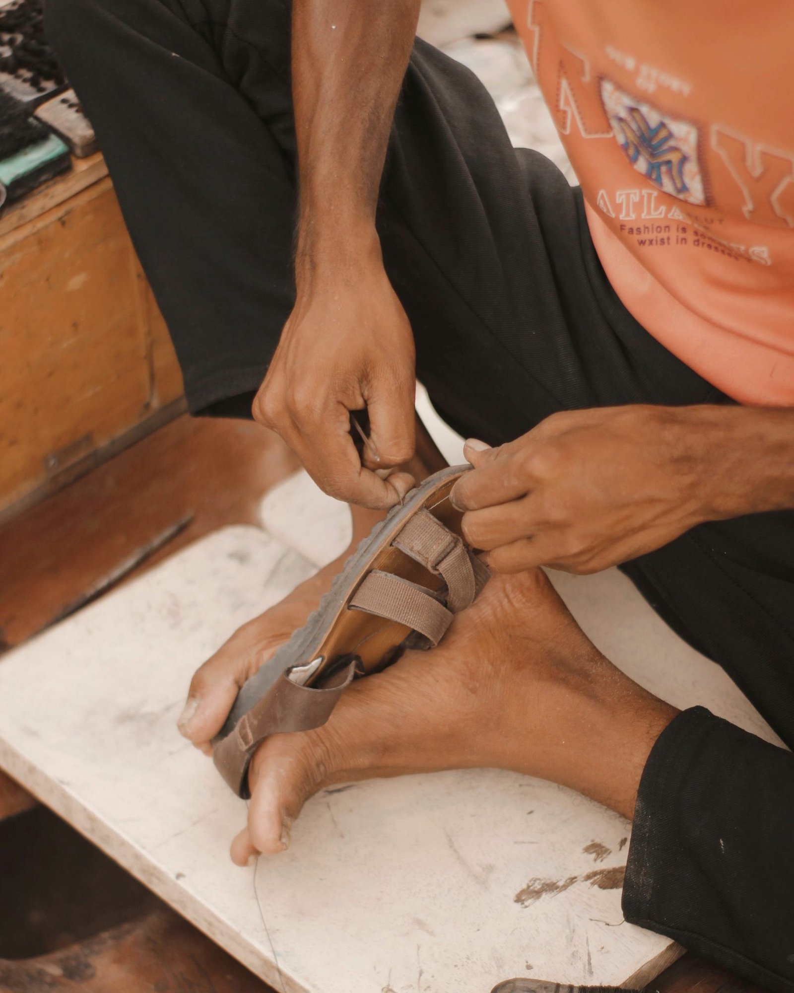 Hands working a leather sole flat against a bench.