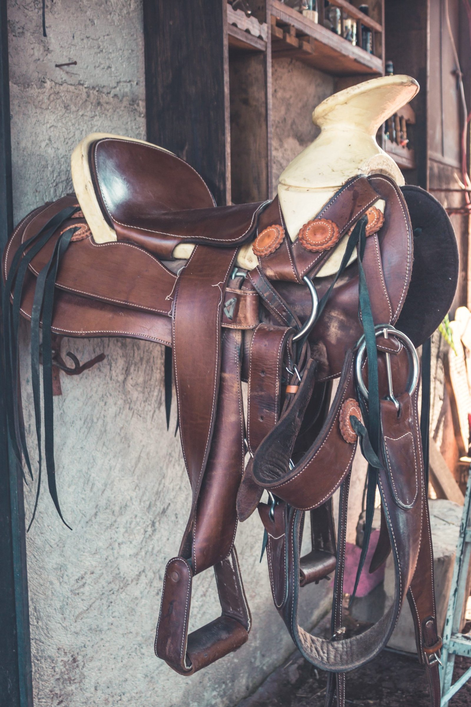 A western saddle hanging on a rack with stirrups and latigo straps.